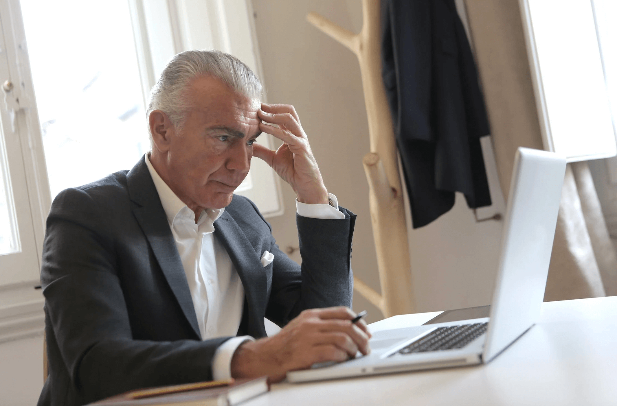Man in a suit looking at a computer with a stressed look.