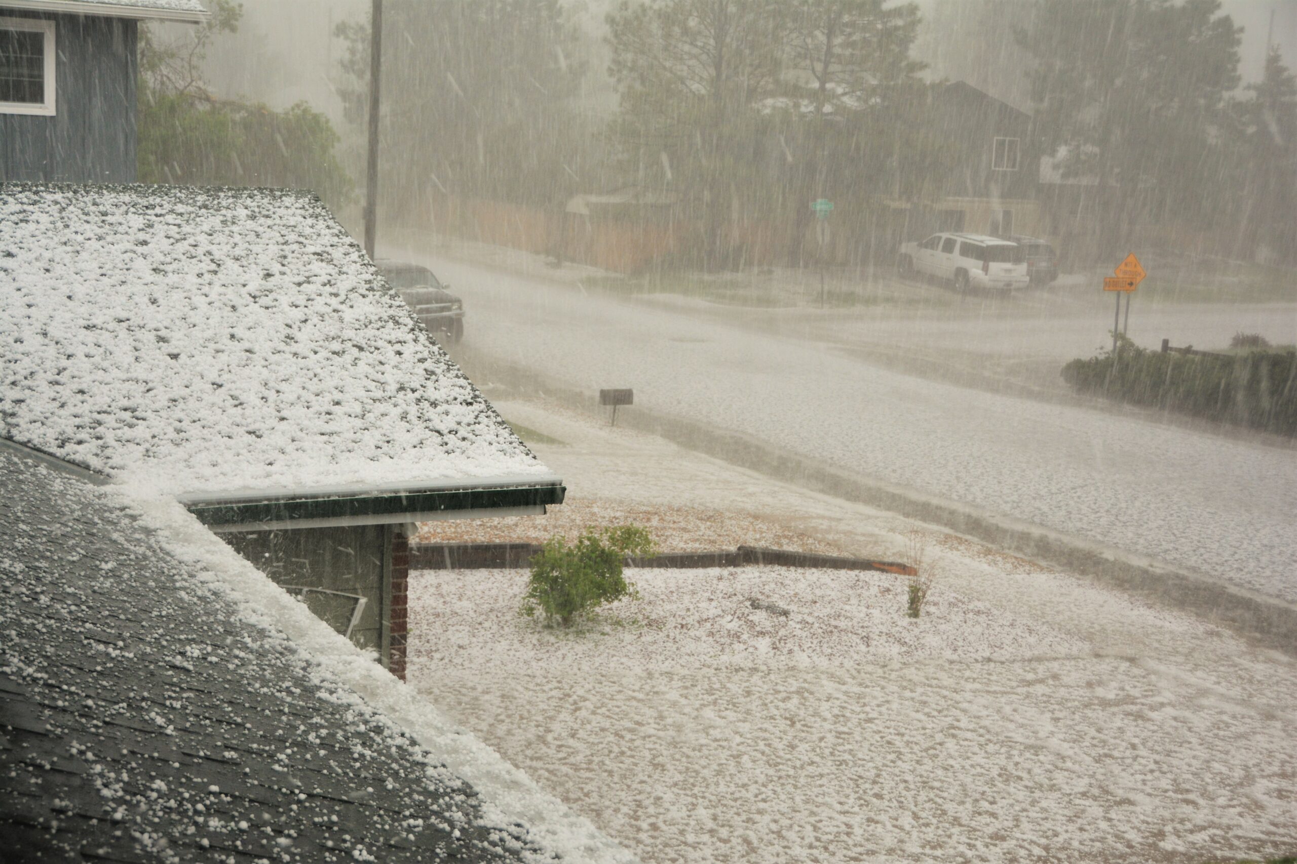 Hailstones all over a roof of a house and neighbourhood street.