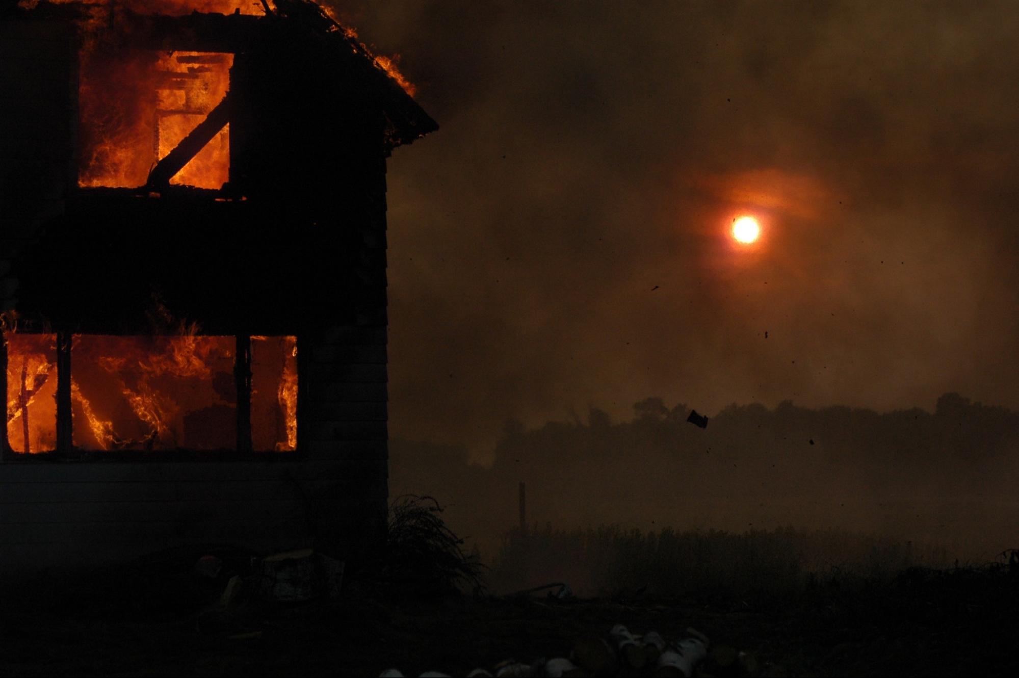 A house on fire with a red moon in the background.