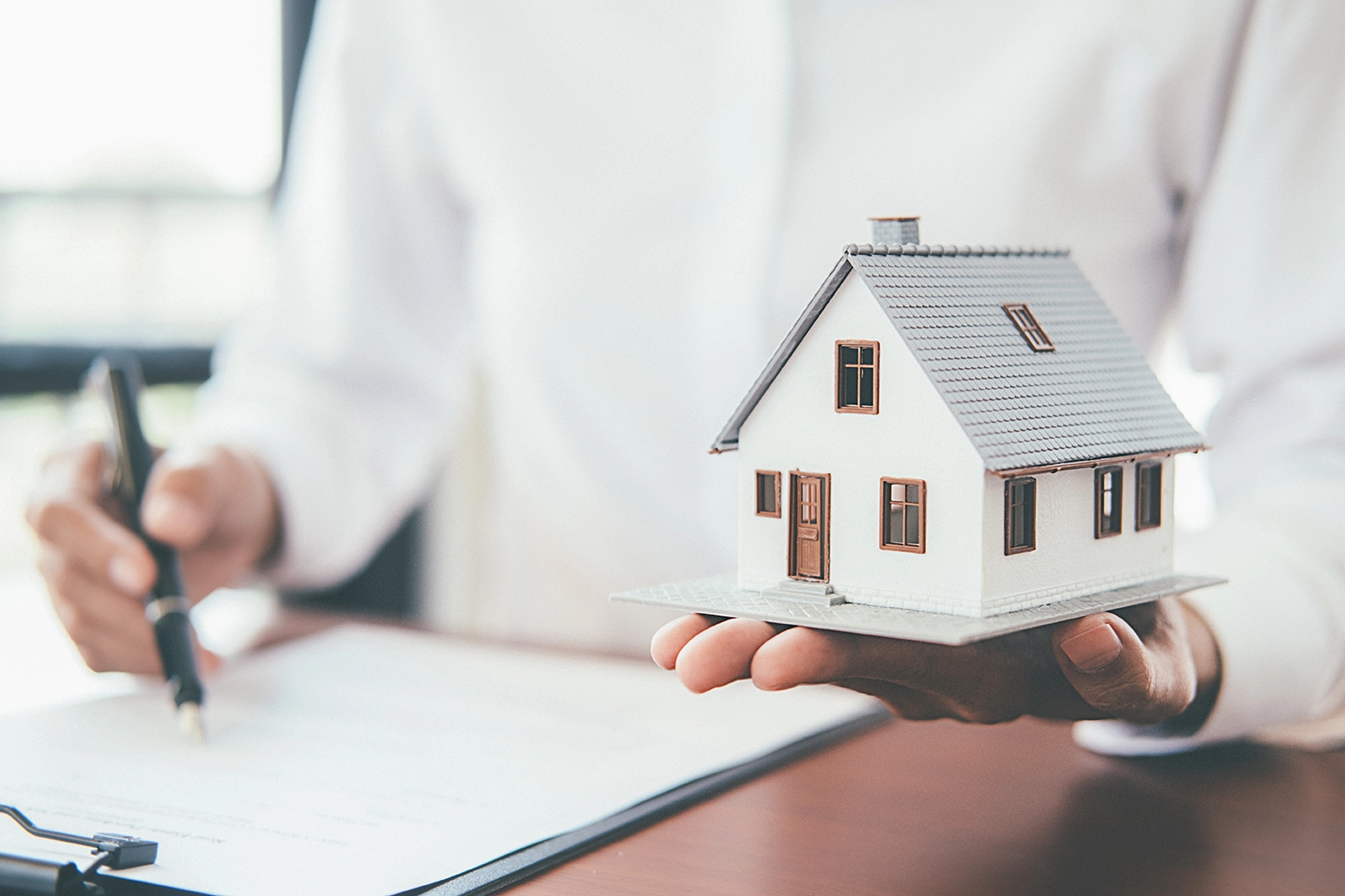 A person holding a toy house while writing on paper.